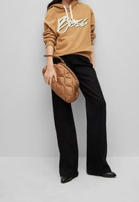 Brązowa bluza z kapturem z białym logo, czarne szerokie spodnie oraz brązowa pikowana torebka. Torebka ma zaokrąglony kształt i fakturowaną powierzchnię.
