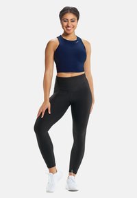 Top corto blu marina con scollo alto, abbinato a leggings neri a vita alta. Sono visibili anche scarpe da ginnastica bianche con lacci.