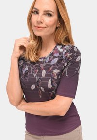 Hemd mit kurzen Ärmeln in Lila mit floralem Muster in verschiedenen Pink- und Lilatönen, glatter Textur und Rundhalsausschnitt.