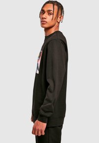 Black sweatshirt with long sleeves, crew neckline, soft texture, and a rectangular graphic print on the chest featuring colorful design elements.