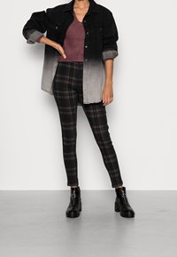 Camicia di denim ombre nera e grigia, maglione di maglia bordeaux, pantaloni skinny a quadri neri e marroni, e stivaletti neri con suola spessa.