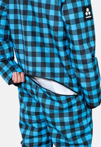 Prenda exterior de cuadros en negro y turquesa con un bolsillo con cremallera, que presenta una textura acolchada y un ajuste moderno. Cuenta con un parche de logotipo en la manga.