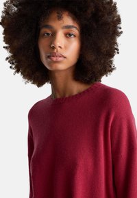 Bordowy, dzianinowy sweter z prążkowanym, okrągłym dekoltem i miękką fakturą. Luźny krój z opuszczanymi ramionami i długimi rękawami.