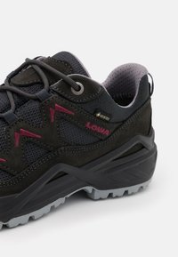 Scarpa da trekking nera e grigia con tomaia in suede e mesh, caratteristiche dettagli rossi, finitura testurizzata e suola in gomma robusta. Etichetta Gore-Tex impermeabile visibile.