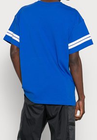 Blå bomulls t-shirt med korta ärmar som har vita ränder på mudden, avslappnad passform och en rundad nederkant baktill.