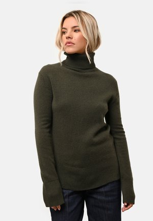Olijfgroene coltrui van gestructureerde stof, met lange mouwen en geribbelde manchetten, gecombineerd met donkere jeans voor contrast.