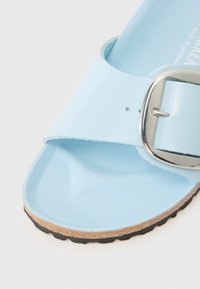 Sandálias azul claro feitas de material brilhante, com uma tira larga com fivela prateada e uma sola de cortiça texturizada com uma borda preta.