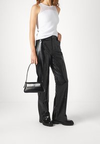 Vit ribbad linne med ett genomskinligt panel, kombinerat med högmidjade svarta byxor i konstläder med en glänsande krokodilmönster och en svart handväska.