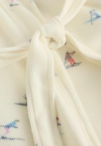 Kremowa prążkowana tkanina z małymi wielokolorowymi wzorami narciarzy, na której znajduje się zbliżenie na związany węzeł.