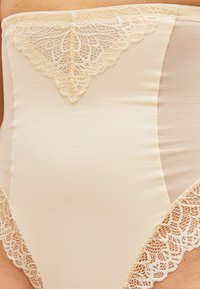 Hoog-gemaakt lichtbeige bikini onderstuk met kantafwerking, voorzien van een mesh paneel aan de zijkant, ontworpen voor comfort en pasvorm.