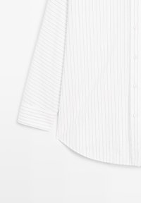 Camicia bianca a maniche lunghe con sottili righe verticali nere, chiusura a bottoni sul davanti, orlo rotondo e texture di tessuto liscia.