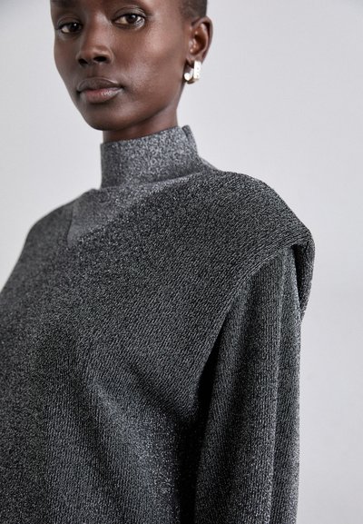Top de cuello alto y mangas cortas en tejido negro texturizado con hilos metálicos. Presenta un diseño de hombros distintivo y un brillo sutil.