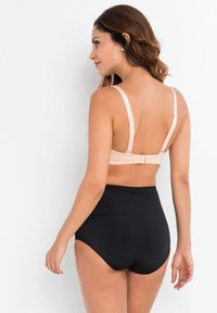 Bralette beige chiaro con spalline regolabili e chiusura a gancio, abbinata a mutandine nere a vita alta, entrambe in tessuti lisci e elasticizzati.