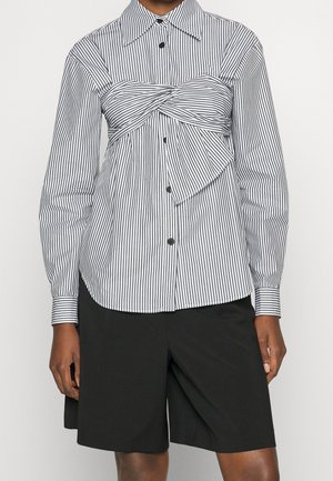 Czarne szorty zestawione z koszulą na guziki w pionowe czarno-białe paski z długim rękawem, ozdobioną skręconym detalem materiału na wysokości klatki piersiowej.
