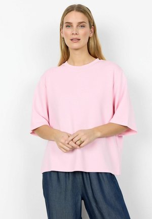 Jasnoróżowa, luźna koszulka oversize z krótkimi rękawami, okrągłym dekoltem i miękkim materiałem; zestawiona z luźnymi, ciemnoniebieskimi spodniami.