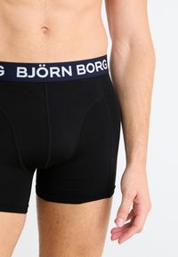 Μαύρα μποξέρ σλιπ με ναυτικό μπλε λωρίδα στη μέση που φέρει λευκή επωνυμία "BJÖRN BORG". Λείος υφασμάτινος χαρακτήρας και εφαρμοστό σχέδιο.
