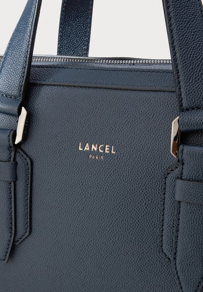 Sac à main en cuir bleu marine avec surface texturée, arborant un logo doré en relief "LANCEL PARIS" et des accents argentés sur les sangles et la fermeture éclair.