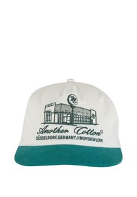 White cap with a green brim, featuring embroidered text and a graphic of a building, labeled "Another Cotton" and "Düsseldorf, Germany."