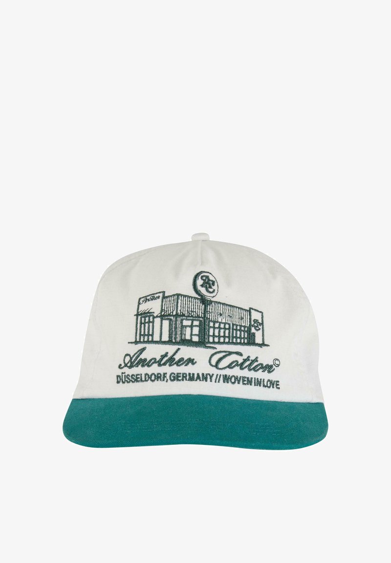 Casquette blanche avec une visière verte, arborant un texte brodé et un graphique d'un bâtiment, étiqueté "Another Cotton" et "Düsseldorf, Allemagne."