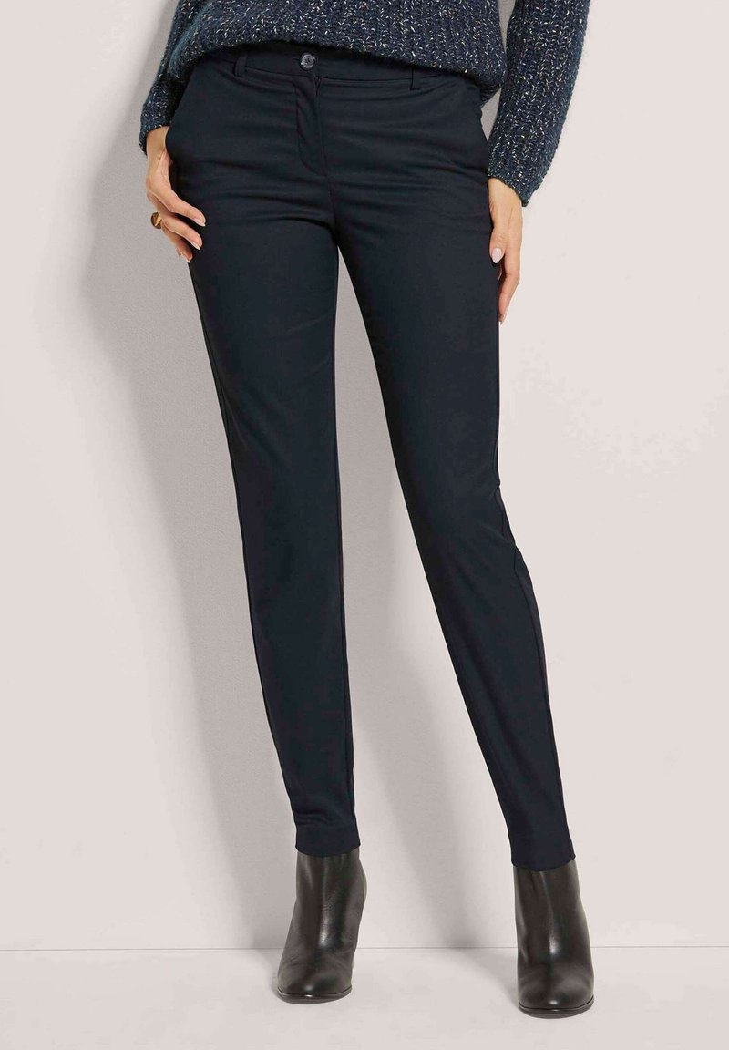 Marineblaue Slim-Fit-Hosen aus glattem Stoff, mit Knopfverschluss, Taschen und einem sauberen Saum. Kombiniert mit schwarzen, hochhackigen Stiefeletten.