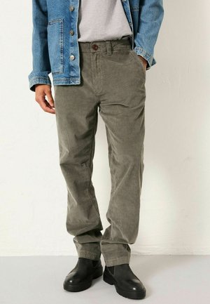 Corduroy pants in olive green with a relaxed fit, featuring a button closure and side pockets, paired with a denim jacket and black boots.