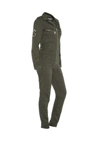 Olijfgroene jumpsuit gemaakt van stevig materiaal. Bevat een ritssluiting aan de voorkant, meerdere zakken en schouderpatches met decoratieve accenten.