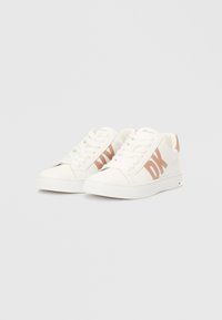 Λευκά αθλητικά παπούτσια με λεία υφή, διακοσμημένα με ένα μπεζ λογότυπο DK στο πλάι, στρογγυλή μύτη και επίπεδη σόλα από καουτσούκ. Έχουν κορδόνια και ελάχιστες σχεδιαστικές λεπτομέρειες.