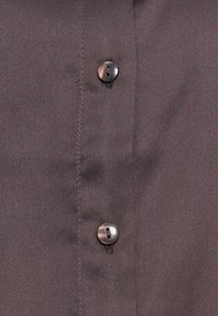 Chemise gris foncé avec une texture lisse, deux boutons noirs et des détails de couture subtils le long de la patte de boutonnage.