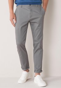 Gray cotton chinos with a slim fit, folded cuffs, and side pockets. Paired with white sneakers, features a smooth texture and minimal design.
