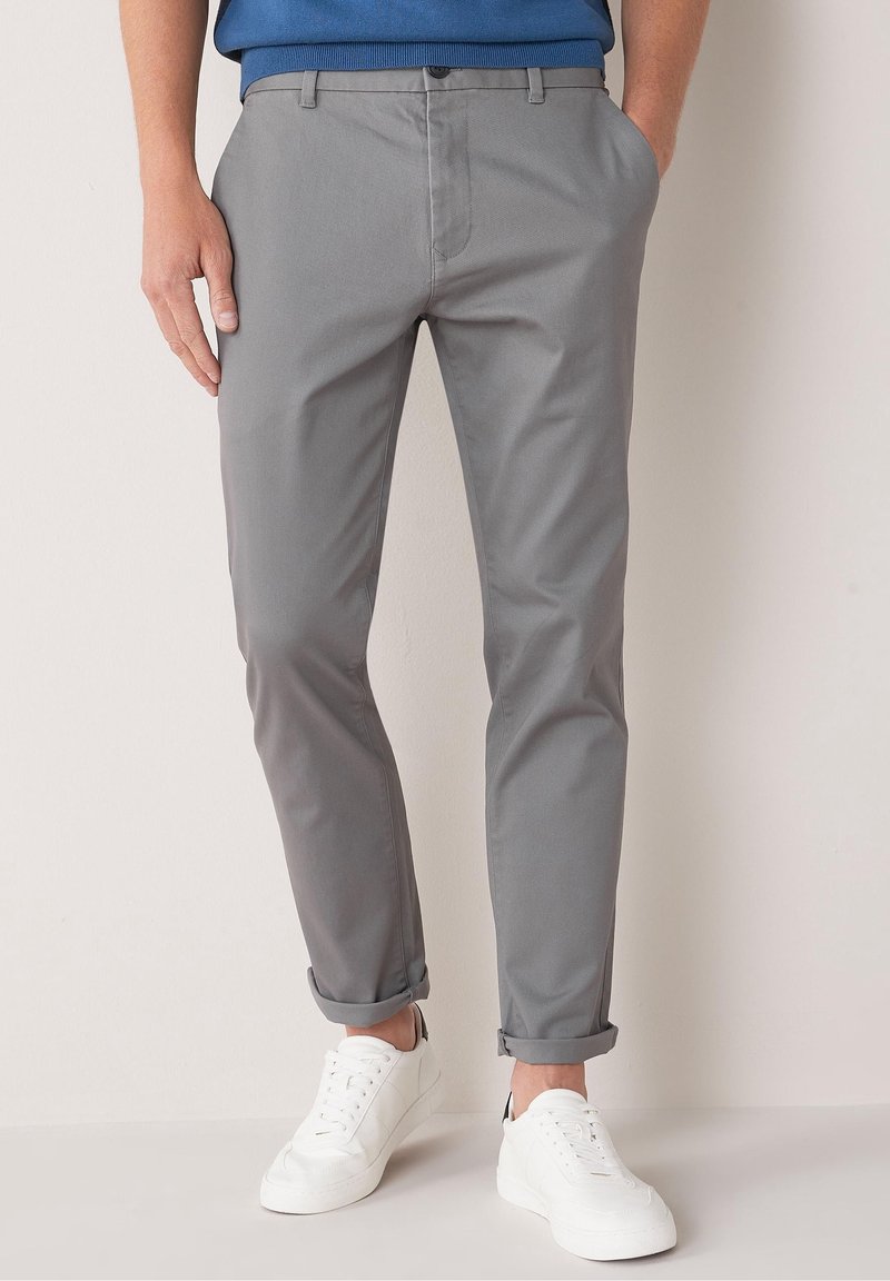 Gray cotton chinos with a slim fit, folded cuffs, and side pockets. Paired with white sneakers, features a smooth texture and minimal design.