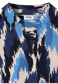 Col de chemise avec motif abstrait de coups de pinceau bleu, marine et beige, et étiquette de la marque CECIL sur un tag blanc à l'intérieur de l'encolure.