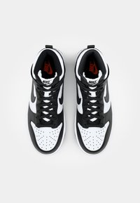 Vysoké tenisky s černým a bílým koženým svrškem, s perforovanou špičkou, černými tkaničkami a červeným logem Nike na vnitřní části.