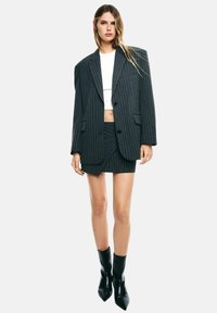 Donna che indossa un blazer oversize a righe e una mini gonna coordinata sopra un crop top bianco, abbinati a stivali neri con punta a coda di rondine.