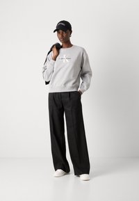 Gray sweatshirt with "Calvin Klein" logo, black wide-leg pants, white sneakers, and a black cap. Simple, casual design with a relaxed fit.