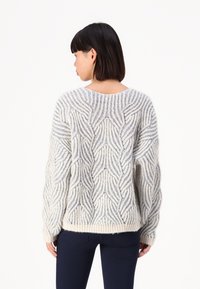 Crème en blauwe gebreide trui met een gestructureerd golfpatroon, verlaagde schouders en geribbelde manchetten, gedragen met donkere marineblauwe broek.