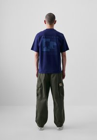 T-shirt marine avec un graphique d'ours et du texte au dos, associé à un pantalon cargo vert olive avec des poches latérales et un patch logo.