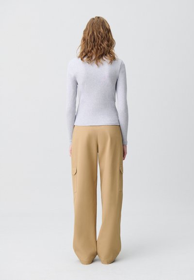 Maglietta fitted a maniche lunghe grigia chiara abbinata a pantaloni ampi beige con tasche laterali duali e una texture di tessuto liscia.