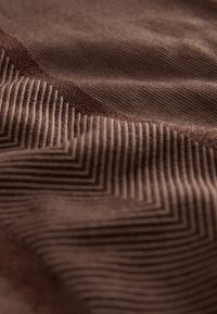 Smeđa tkanina s izdignutim geometrijskim cik-cak i prugastim uzorcima koji stvaraju teksturirane valove.