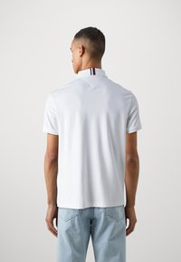 Polo bianco a maniche corte, con colletto a contrasto con strisce rosse e blu navy. Realizzato in un tessuto liscio e traspirante.