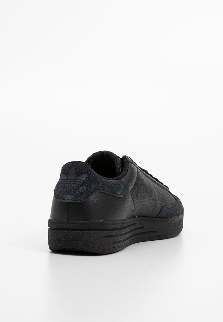 Czarne skórzane sneakersy z zamszowym elementem na pięcie, z wytłoczonym logo Adidas na pięcie oraz grubą teksturowaną podeszwą, przedstawione z tylno-prawej strony na białym tle.