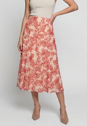 Donna che indossa una gonna pesca a vita alta di lunghezza midi con stampa floreale rossa, abbinata a una canottiera beige senza maniche e tacchi a punta color nudo.