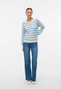 Pull rayé en bleu clair et crème, fabriqué dans un matériau doux, avec une coupe décontractée. Assorti à un jean évasé bleu et des chaussures blanches.