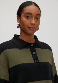 Strickpullover mit abwechselnden dunkelgrünen und schwarzen Streifen, einem Kragen-Halsausschnitt und vier schwarzen Knöpfen auf der Vorderseite.