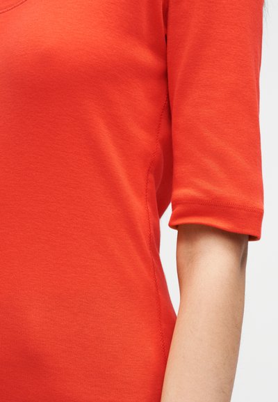 Κόκκινο βαμβακερό τοπ με κοντά μανίκια και στρογγυλή λαιμόκοψη. Διαθέτει λεία υφή και λεπτομέρειες ραφής κατά μήκος των ραφών.