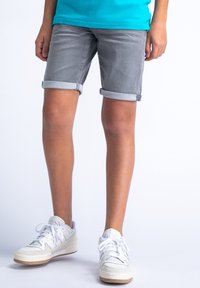 Šedé denimové šortky s ohrnutými manžetami, doplněné bílými teniskami se šedými akcenty a texturovanými panely. Model stojí na světlejším pozadí.