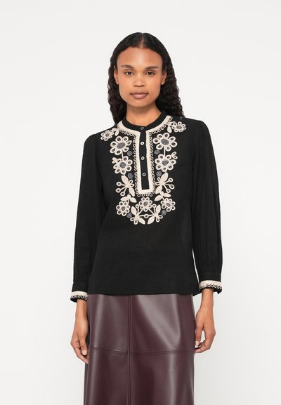 Chemise noire à manches longues avec broderie florale crème, col, patte de boutonnage et poignets décoratifs. Le matériau a une apparence texturée.