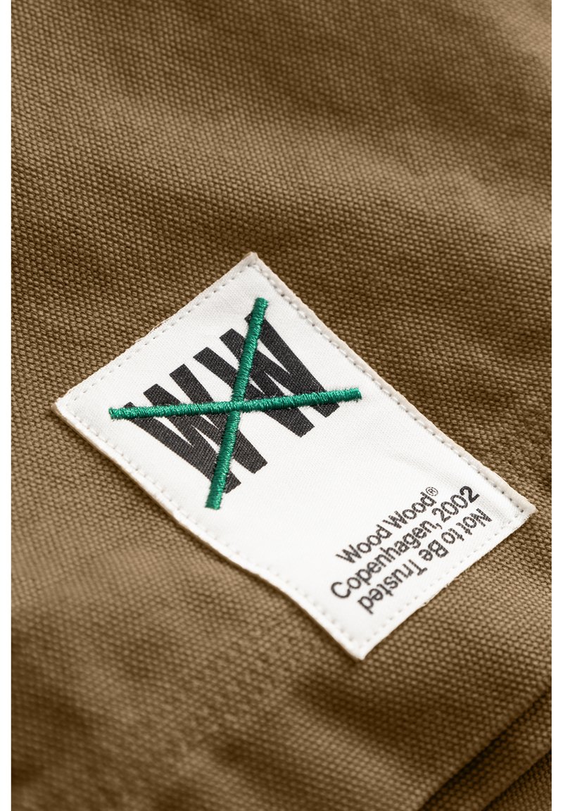 Tissu brun à l'apparence texturée comportant une étiquette blanche avec un texte noir et des accents verts cousus, dont une ligne diagonale.