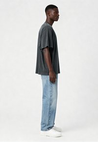 Aizsargājoša pelēka t-krekla ar īsām piedurknēm, brīvā piegriezumā, apvienota ar gaiši ziliem džinsiem un baltām sporta apaviem. Audums izskatās mīksts, ar nedaudz nodilumu tekstūru.