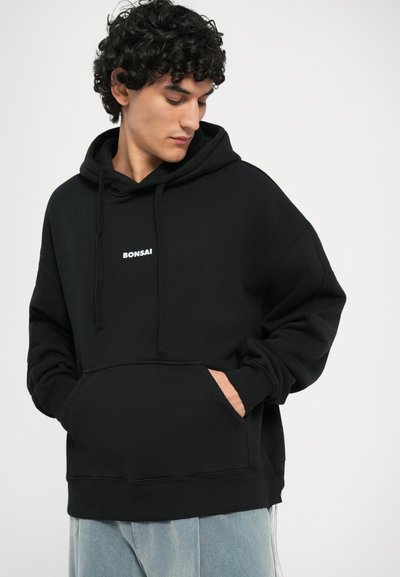 Zwarte hoodie met een voorzak, trekkoordcapuchon en wit "Bonsai" logo op de borst. Zacht materiaal met een relaxte pasvorm.