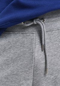 Grå sweatpants med en ribbet talje og snøre, der har metalliske spidser. En blå sweatshirt dækker delvist taljen.